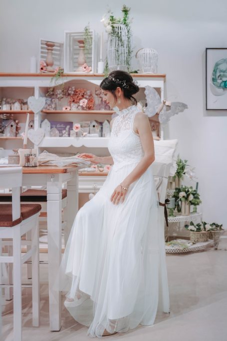 Braut in einem weißen Kleid, sitzt an einem Tisch in einem hellen, dekorierten Raum.