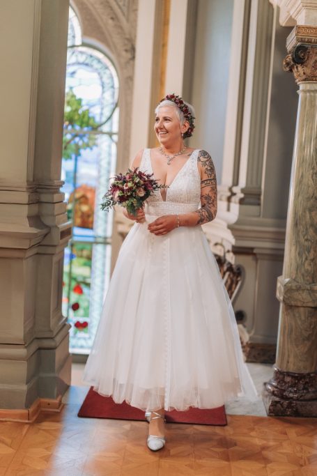 Braut in einem weißen Kleid mit Blumenstrauß steht in einer Kirche.