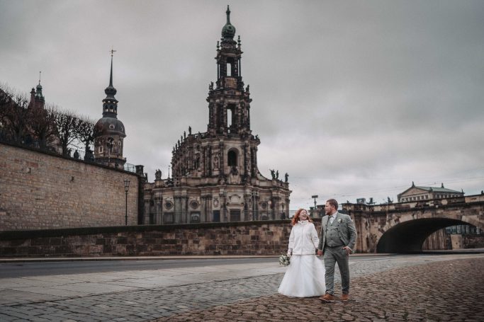 Hochzeitspaar vor historischer Architektur in Dresden unter bewölktem Himmel.