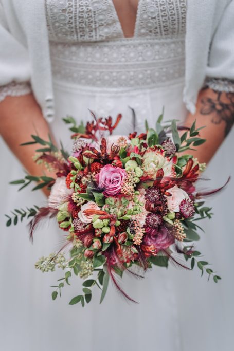 Braut hält einen bunten Blumenstrauß mit rosa, roten und grünen Blüten.